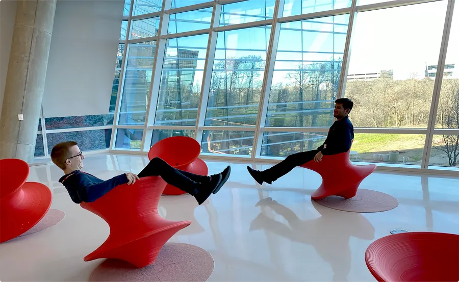 Two men sitting on spinning top red chairs.
